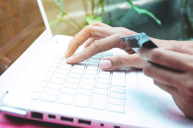 Foto gekapte handen van een vrouw met een creditcard met een laptop op tafel