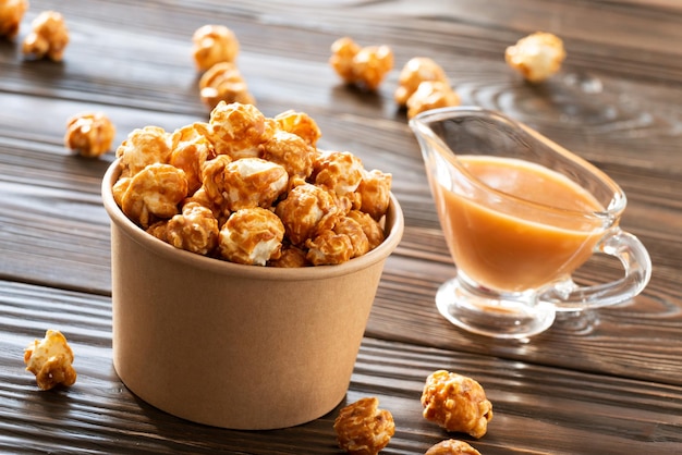 Gekarameliseerde popcorn in papieren emmer op houten tafel