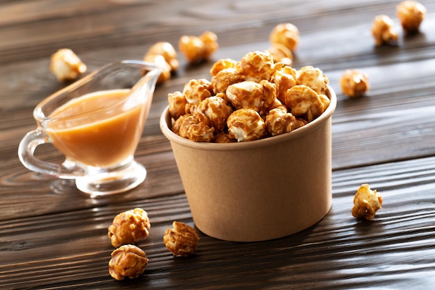 Gekarameliseerde popcorn in papieren emmer op houten tafel