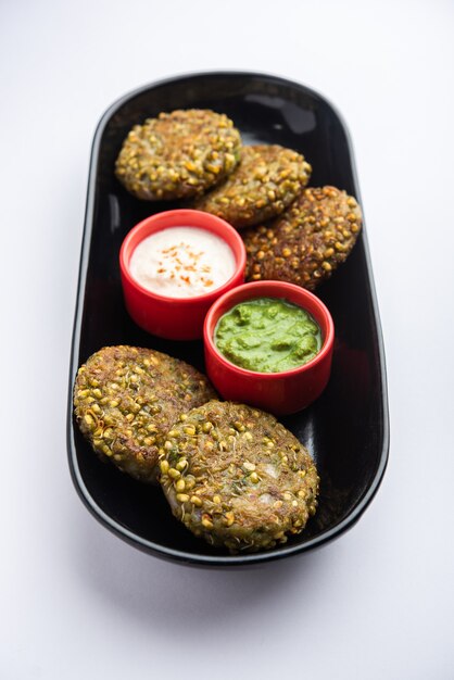 Gekiemde moong dal tikki of pasteitjes is een gezonde snack uit India geserveerd met groene chutney en wrongel