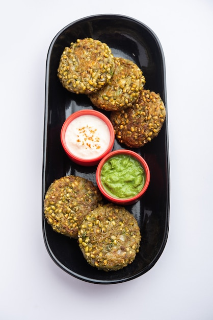 Gekiemde moong dal tikki of pasteitjes is een gezonde snack uit India geserveerd met groene chutney en wrongel