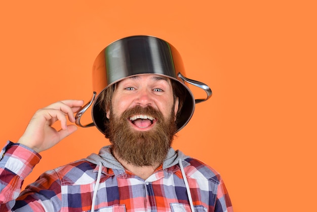 Foto gekke chef-kok met pan op hoofd lachende man chef-kok met pot steelpan koken keukengerei koken