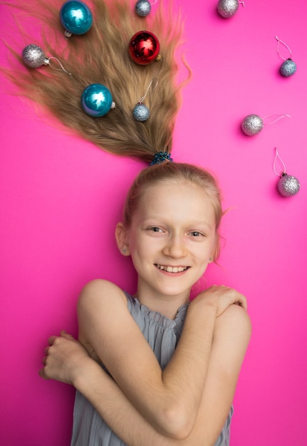 Gekke gelukkige en heldere nieuwjaarsvakantie. meisje met kerstballen op roze achtergrond