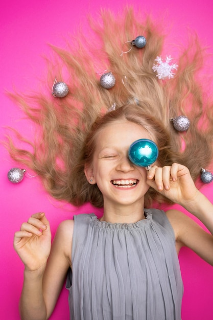 Gekke gelukkige en heldere nieuwjaarsvakantie. meisje met kerstballen op roze achtergrond