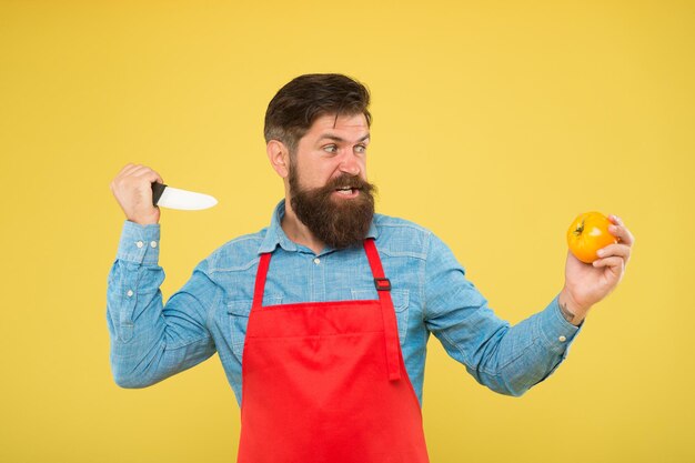 Gekke kok. Ultieme lijst met snijtechnieken die elke chef zou moeten kennen. Bebaarde man bereiden tomaat. Veilig snijden. Groenten snijden. Salade recept. Volwassen man houdt mes en groente vast. Agressie concept.