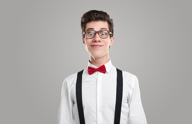 Gekke mannelijke nerd in een wit overhemd en een bril die lacht en naar de camera kijkt tegen een grijze achtergrond