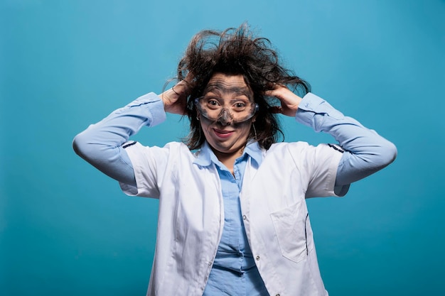 Gekke scheikundige met een gek uiterlijk die zich schuldig voelde voor een explosie, was het gevolg van een mislukt chemisch experiment. Gekke wetenschapper met rommelig haar, vies gezicht en domme uitdrukking op blauwe achtergrond.