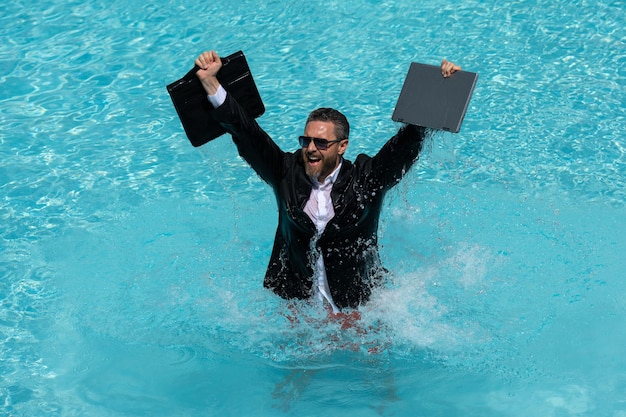 Gekke zakenman in een pak werkt voor een laptop die in het water staat in zwembad op afstand c