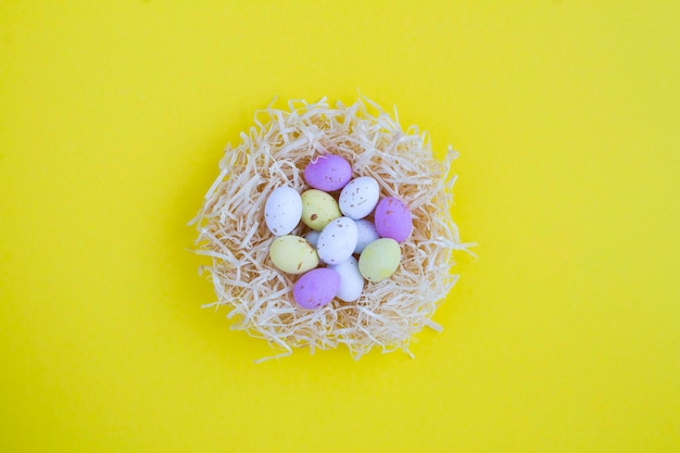 Gekleurde paaseieren in een nest van stro op de gele achtergrond close-up bovenaanzicht