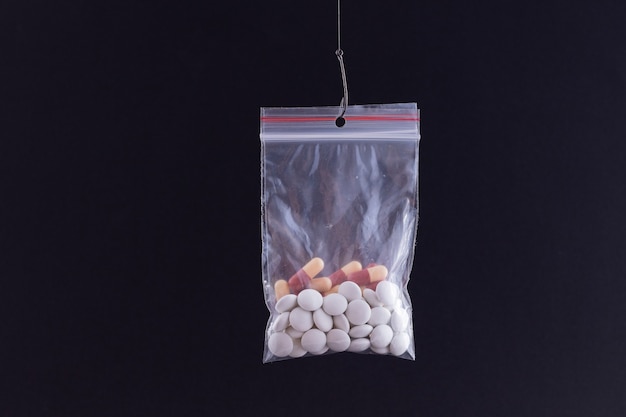 Gekleurde pillen of tabletten die in een kleine ritssluitingszak aan een vishaak hangen