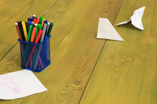 Gekleurde stiften in een blauwe metalen doos. Vellen papier op een geelgroene ondergrond