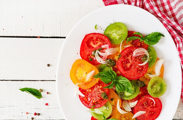 Gekleurde tomatensalade met ui en basilicumpesto.