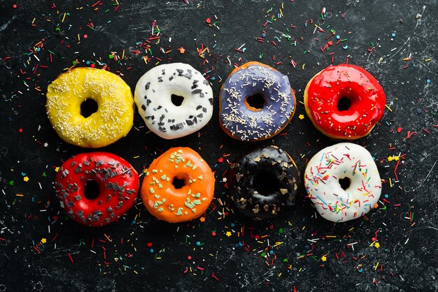 Gekleurde zoete gebakken donuts op een zwarte achtergrond Bovenaanzicht Rustieke stijl