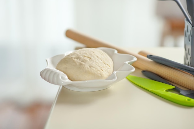 Gekneed deeg in een witte kom op een keukentafel met keukengerei