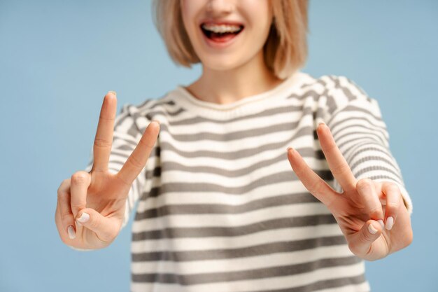 Foto geknipte afbeelding van de vreugdevolle blonde vrouw die het overwinningsteken toont met twee handen geïsoleerd