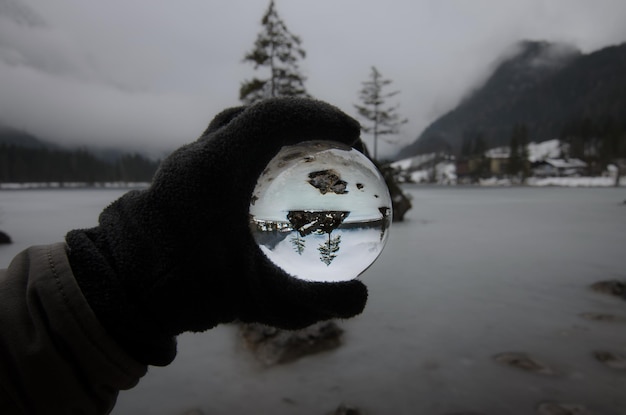 Foto geknipte hand met kristallen bol bij de reflectie van het meer in de winter