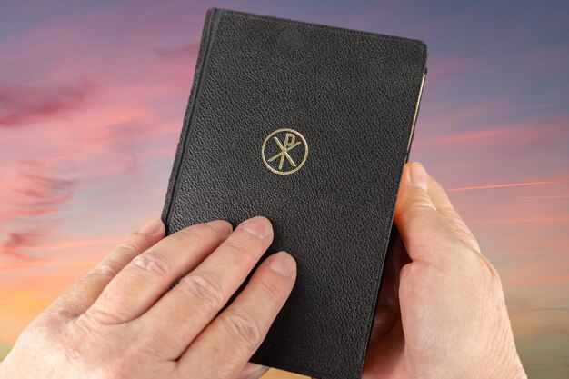 Geknipte handen met een bijbel tegen de hemel bij zonsondergang