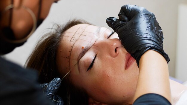 Foto geknipte handen van een schoonheidsspecialist die de wenkbrauw van een vrouw draagt.