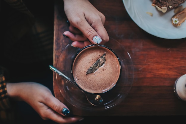Geknipte handen van een vrouw met een koffiekop op een houten tafel
