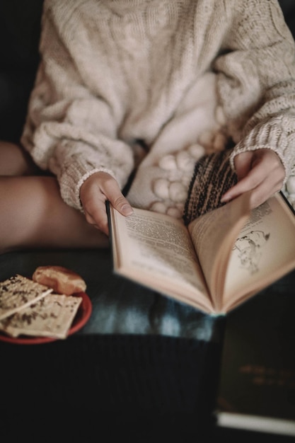 Foto geknipte jonge vrouw in een gezellige gebreide trui die een boek leest op het bed thuis esthetiek winter