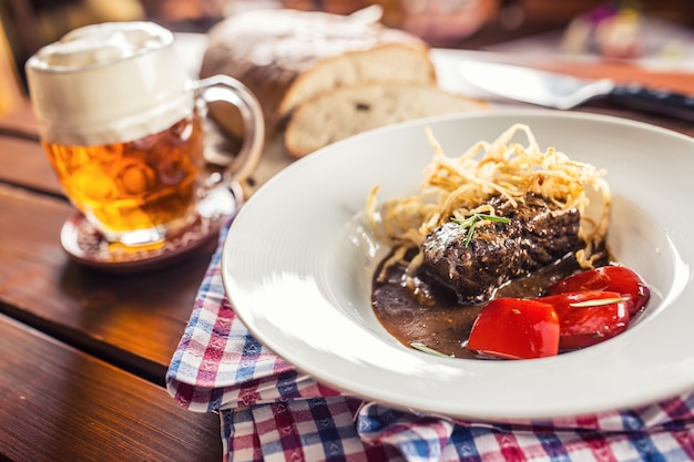 Gekonfijte biefstuk met saus gebakken ui brood tapbier en decoratie in café of restaurant.