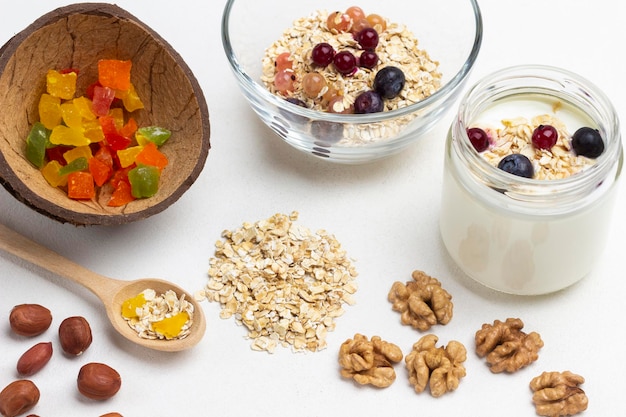 Gekonfijte vruchten in een kokosnootschaal. Havermout en noten op tafel. Havermout en yoghurt in glazen pot. Witte achtergrond. Bovenaanzicht