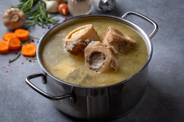 Foto gekookt bot en bouillon. zelfgemaakte runderbottenbouillon wordt gekookt in een pot op. botten bevatten collageen, dat het lichaam voorziet van aminozuren, de bouwstenen van eiwitten.