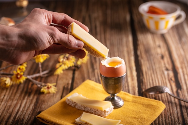 Gekookt ei in een zilveren eierdopje met brood en kaas op een houten tafel