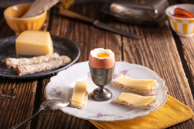 Gekookt ei in een zilveren eierdopje met brood en kaas op een houten tafel