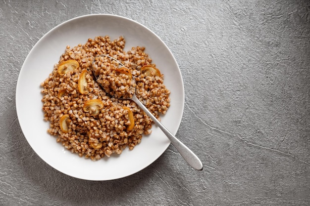 Gekookte boekweitpap met champignons met een lepel op een grijze tafel