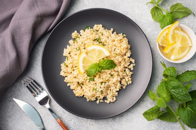 Gekookte bulgur met verse citroen en munt op een bord. Een traditioneel oosters gerecht genaamd Tabouleh. Grijze betonnen achtergrond