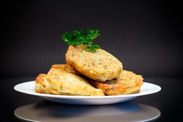 gekookte gebakken aardappelkotlets met kruiden in een plaat geïsoleerd op een zwarte achtergrond