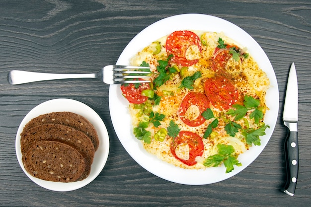 Foto gekookte gebakken omelet met kruiden en groenten in een witte plaat op een houten tafel