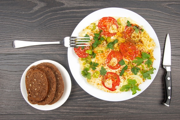 Gekookte gebakken omelet met kruiden en groenten in een witte plaat op een houten tafel