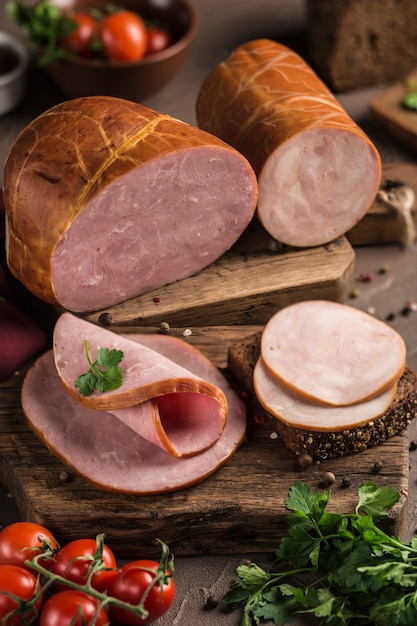 Gekookte ham gesneden op brood ligt op een houten bord met verse kruiden en kerstomaatjes. Donkere achtergrond. Zijaanzicht. Verticale oriëntatie.