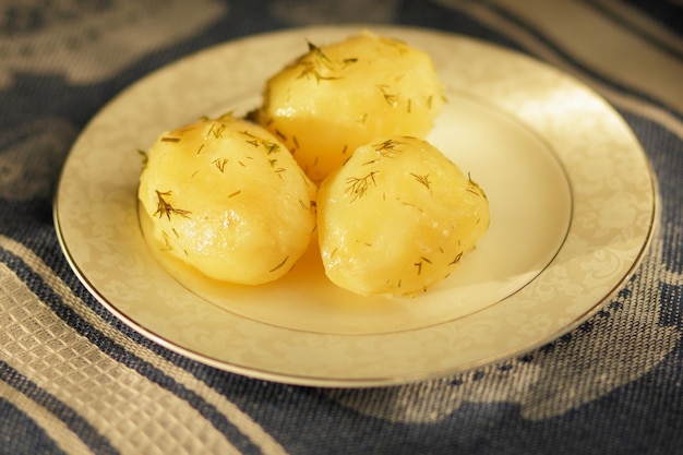 Gekookte jonge aardappelen met dille op een witte plaat Vegetarisch voedselconcept Close-up van aardappelen op een blauw servet