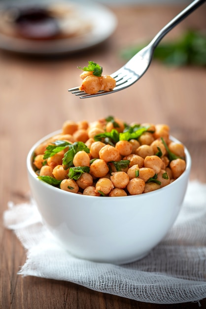 Gekookte kikkererwten met peterselie en paprika in een witte kom. Vegetarisch eten.