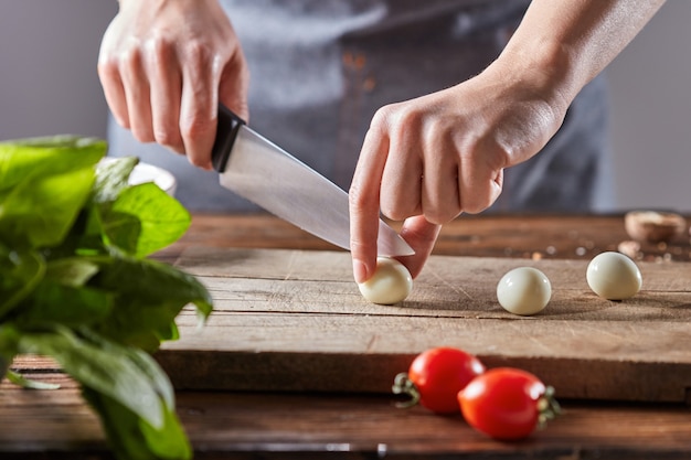 Gekookte kwarteleitjes snijden vrouwelijke handen op een houten bord op een tafel met tomaten en spinazie. Stap voor stap voorbereiding