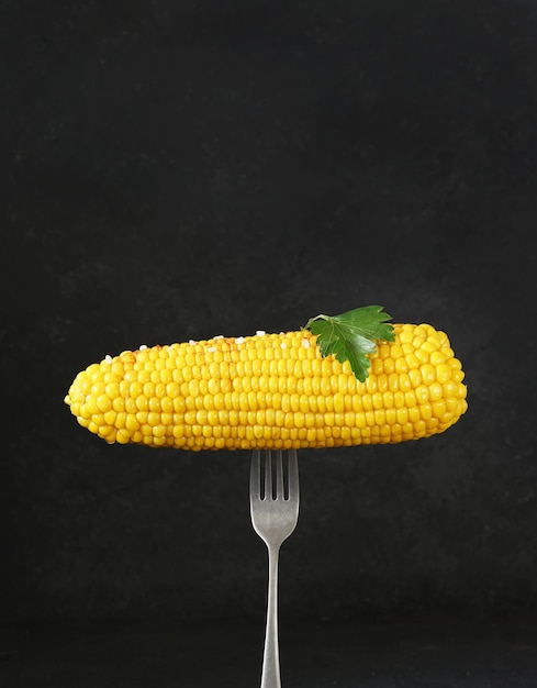 Gekookte maïs op de vork met zout en peterselieblad op donkere backround kopie ruimte