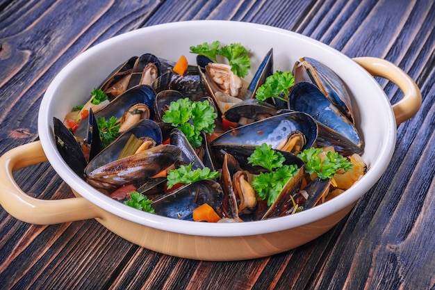 Gekookte mosselen in het koken van schotel met peterselie op een houten achtergrond