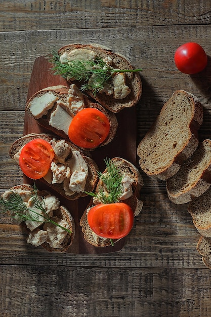 Gekookte sandwiches met kabeljauwlever, tomaten en kruiden op een houten ondergrond