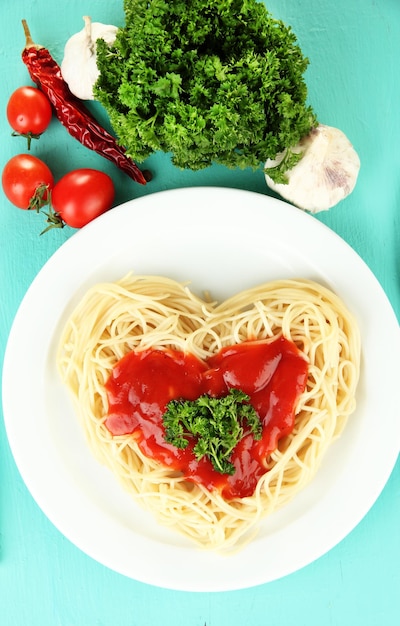 Gekookte spaghetti zorgvuldig gerangschikt in hartvorm en gegarneerd met tomatensaus, op blauwe achtergrond