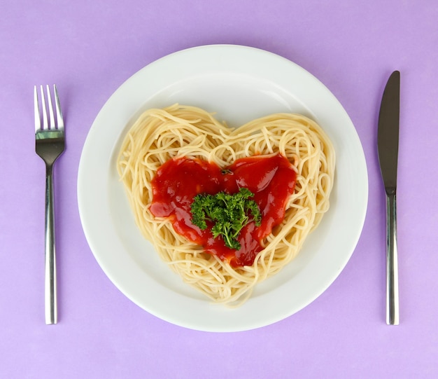 Gekookte spaghetti zorgvuldig gerangschikt in hartvorm en gegarneerd met tomatensaus, op kleur achtergrond