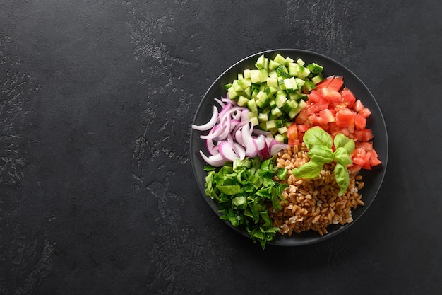 Gekookte volkoren speltsalade met seizoensgroenten in kom op zwarte achtergrond.