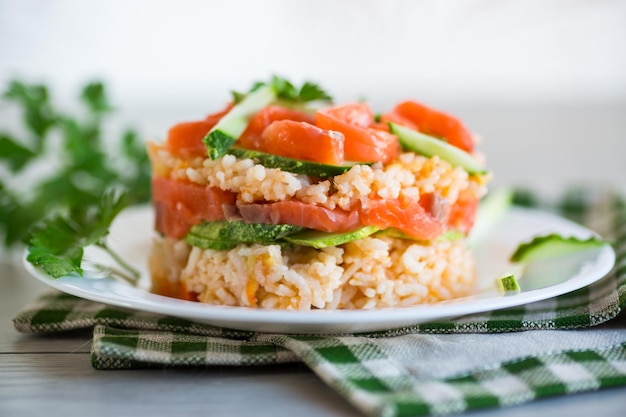 Gekookte witte rijst met gezouten rode vis komkommers en andere groenten met kruiden in een bord op een houten tafel