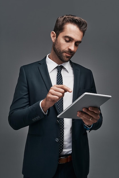 Gekoppeld aan de bedrijfswereld Studio-opname van een knappe jonge zakenman die een digitale tablet gebruikt tegen een grijze achtergrond