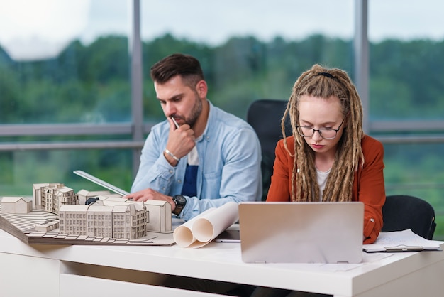 Gekwalificeerde hardwerkende creatieve mannelijke en vrouwelijke ontwerpers die werken met mock-up van gebouwen