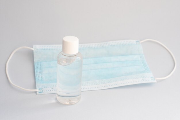 Гель-дезинфицирующее средство в пластиковой бутылке и защитная маска на синем фоне