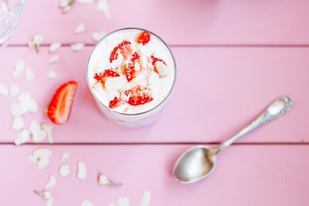 gelaagd zomerdessert met aardbeien, biscuitgebak en yoghurt op een roze boomachtergrond.