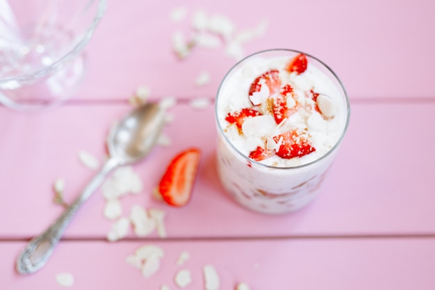 gelaagd zomerdessert met aardbeien, biscuitgebak en yoghurt op een roze boomachtergrond.